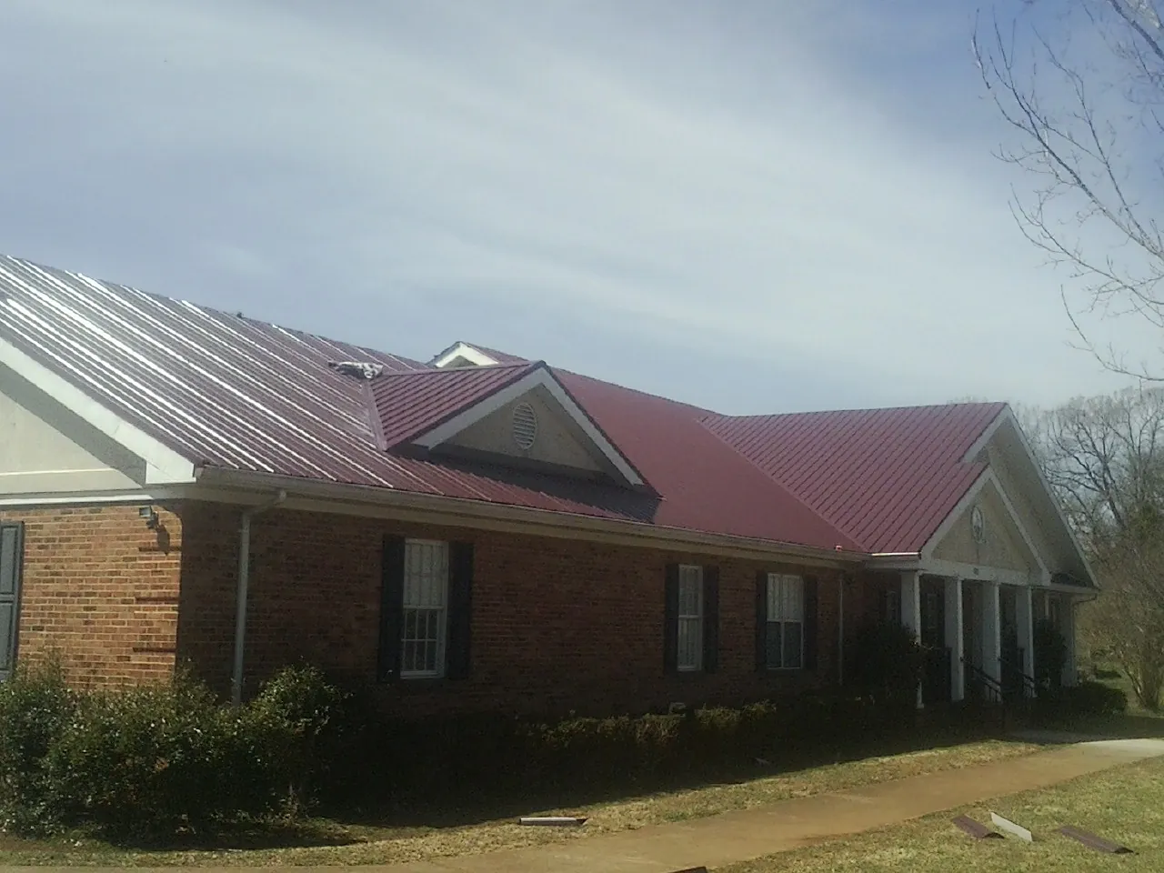 Red metal roof with gabled entries on a long brick building, from a Hail Damage Roof Repair job in New Milford