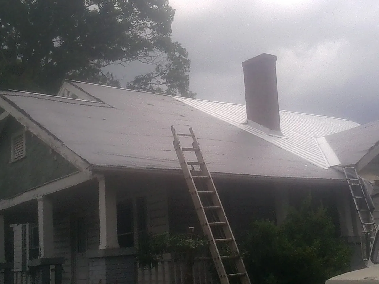 Ladders against a metal roof on an older home with a brick chimney in New Milford
