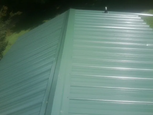 New green metal panels meeting at the ridge of a roof — Flat Roof Repair work by our crew in New Milford