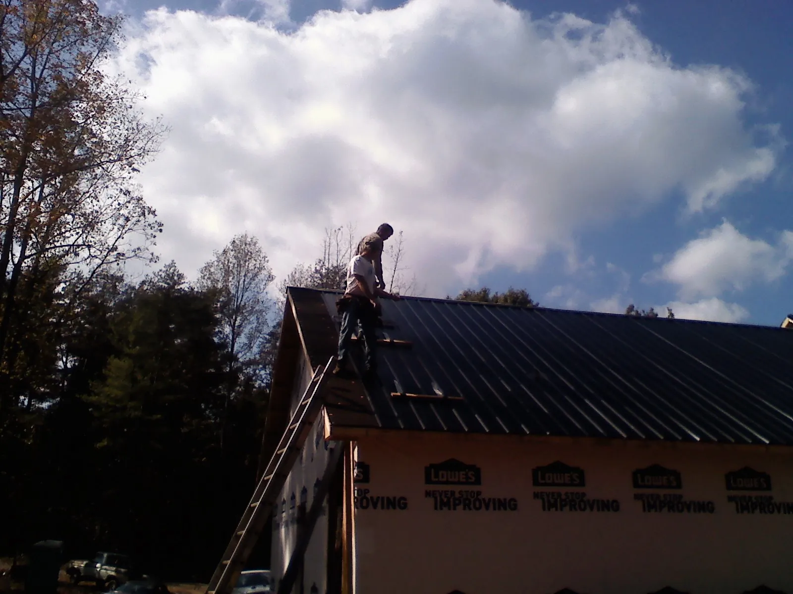 Roofer fastening dark metal panels high against a cloudy sky, from a Roof Inspection job in New Milford